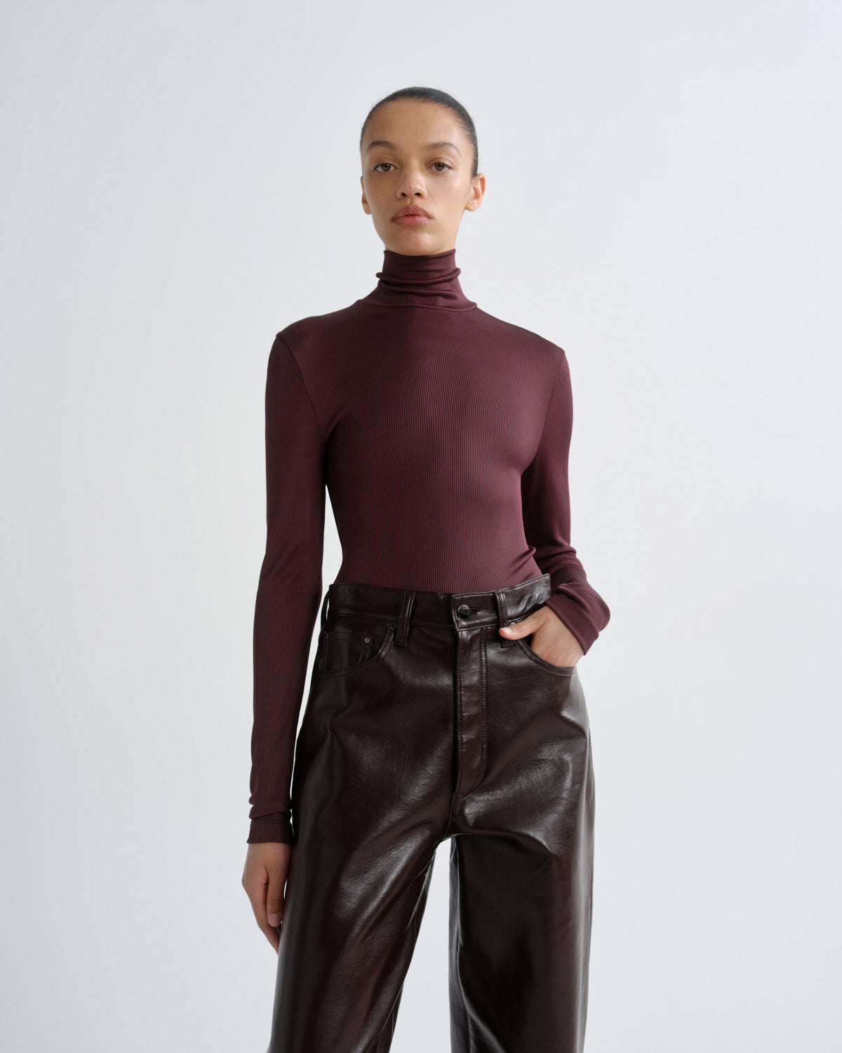 Person wearing a burgundy turtleneck and leather pants on a white background