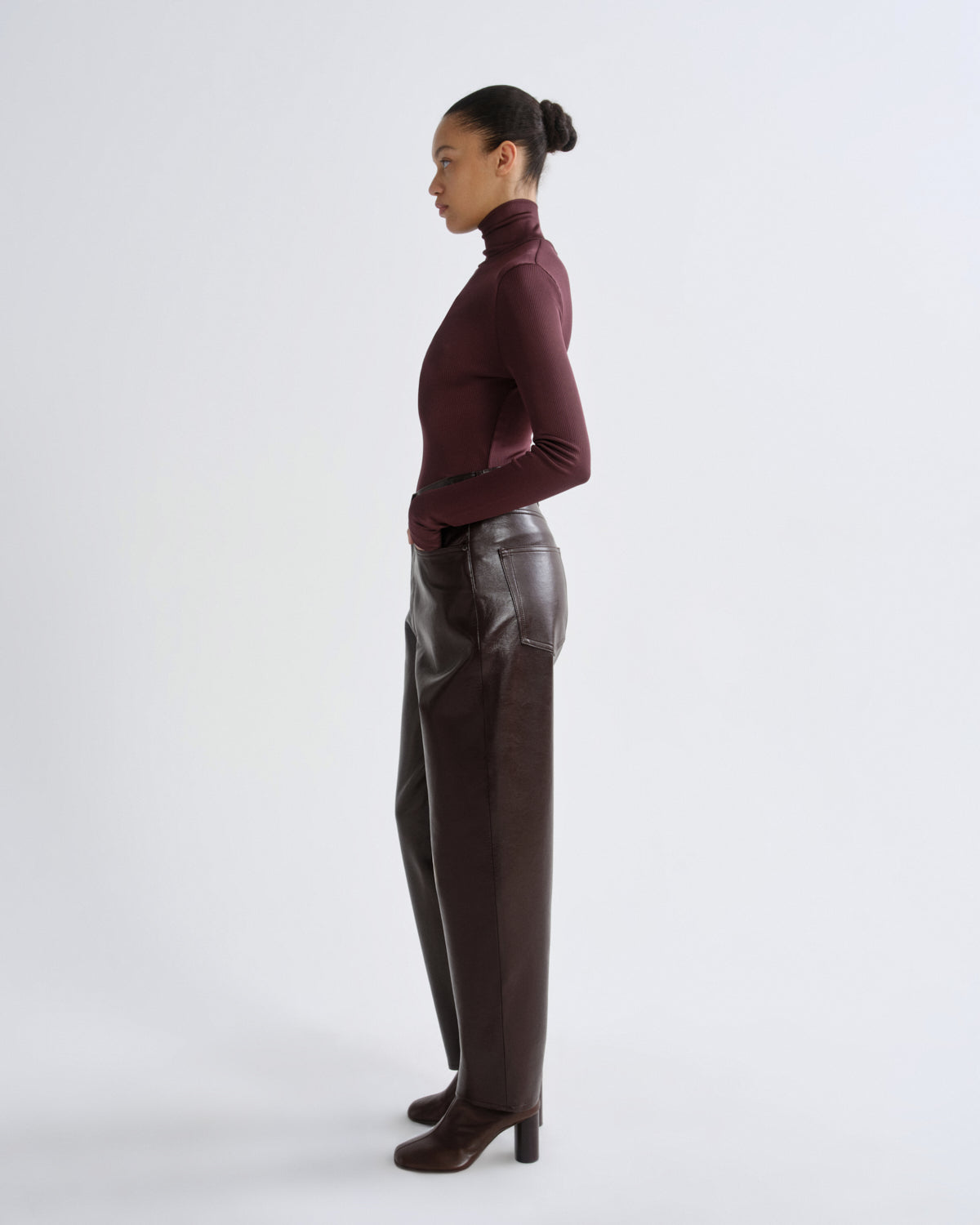 Person wearing a burgundy turtleneck and leather pants on a white background