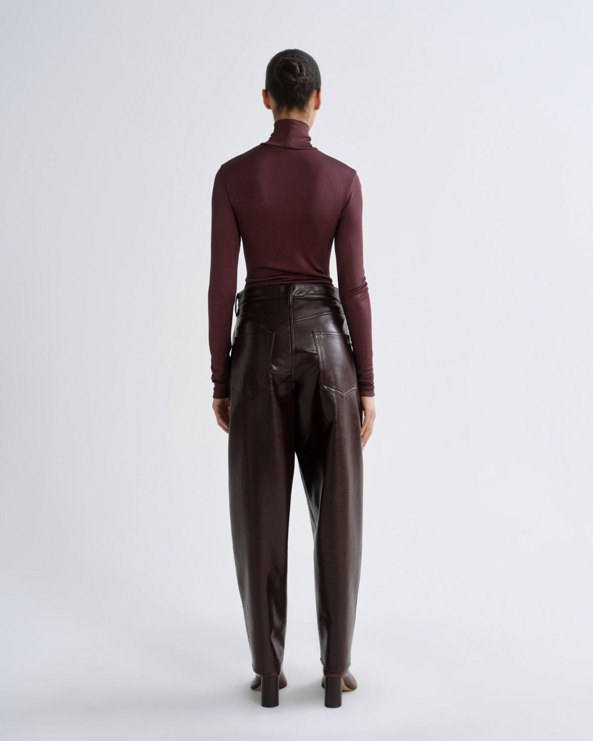 Person wearing a burgundy turtleneck and brown leather pants on a white background