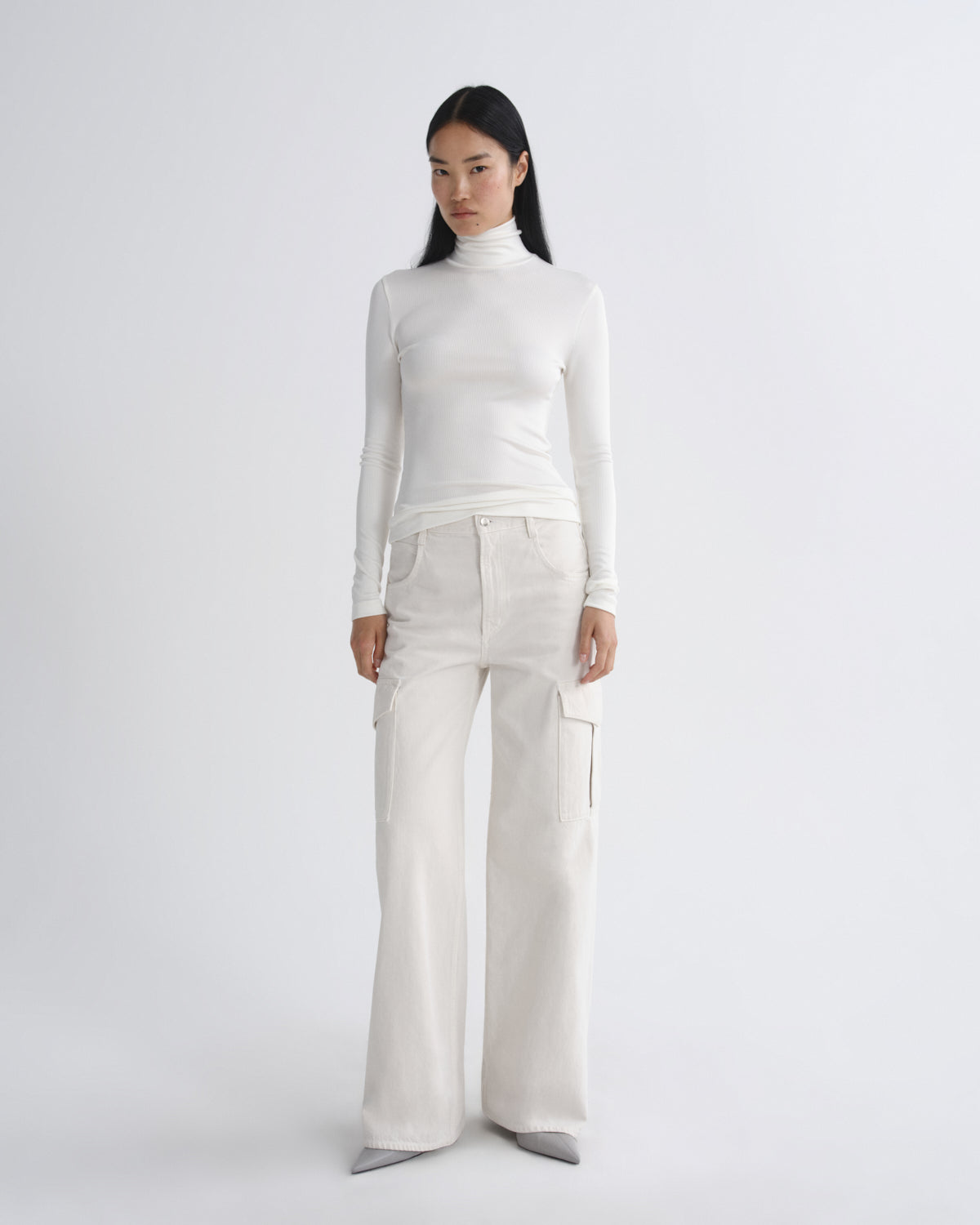 Person wearing a white turtleneck and cream pants on a light gray background