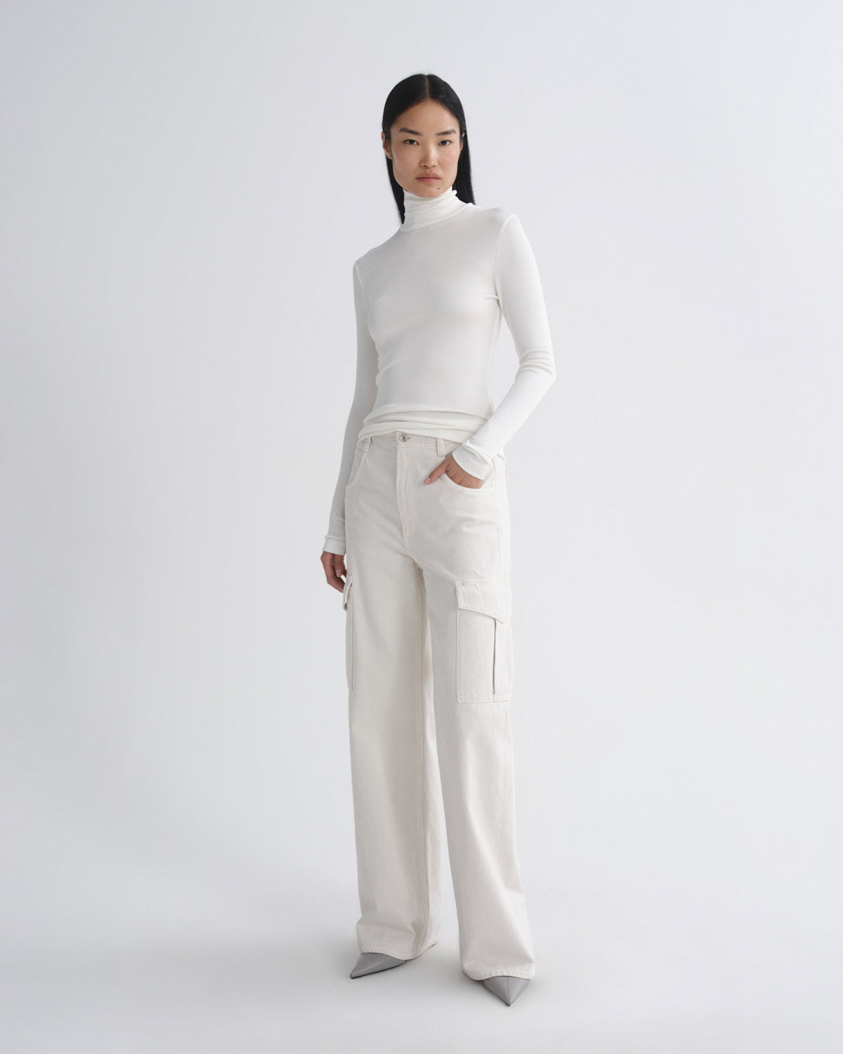 Woman wearing a white turtleneck and beige pants on a white background