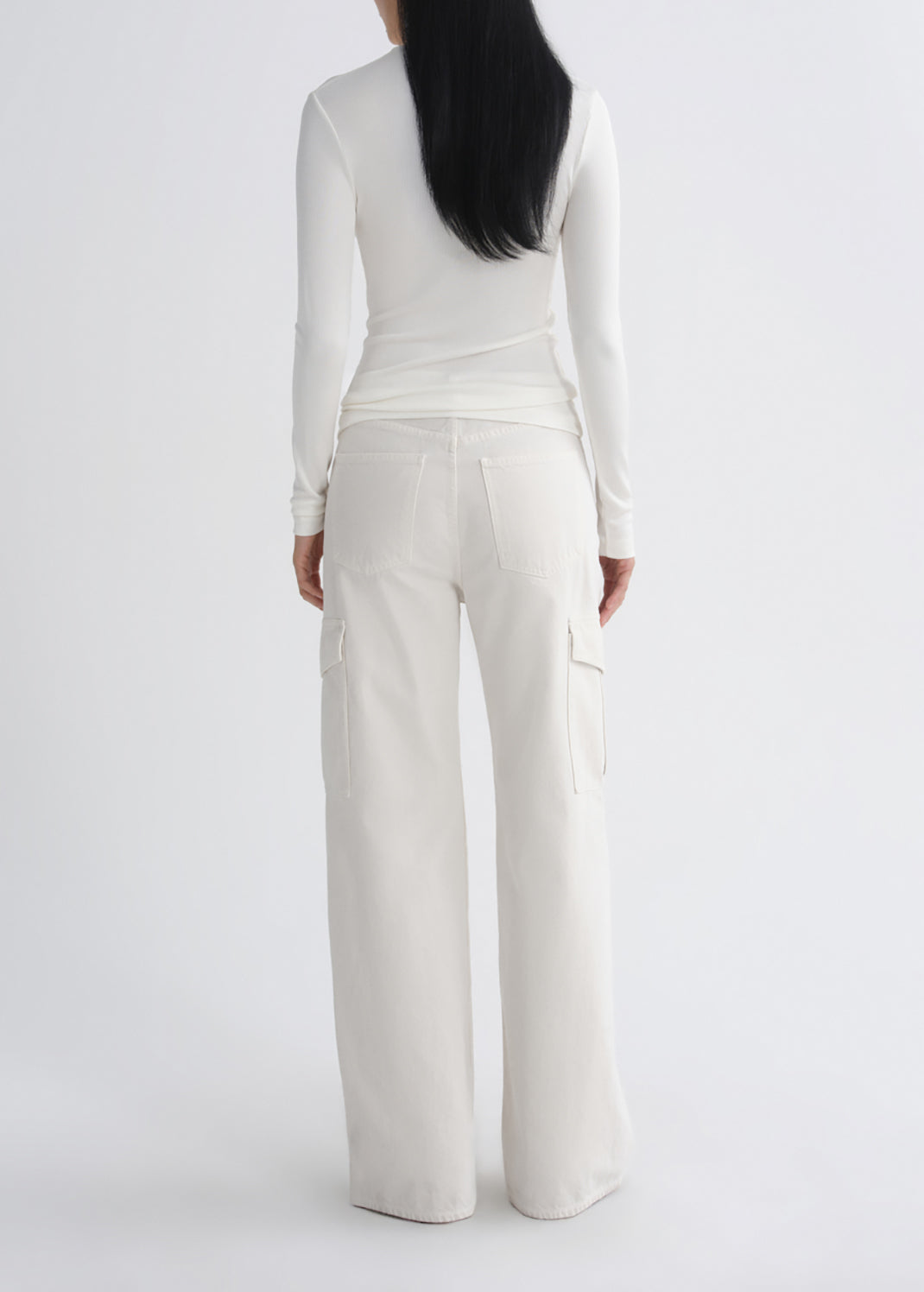 A model viewed from the back wearing a white long-sleeve top and matching white wide-leg cargo pants against a grey background.