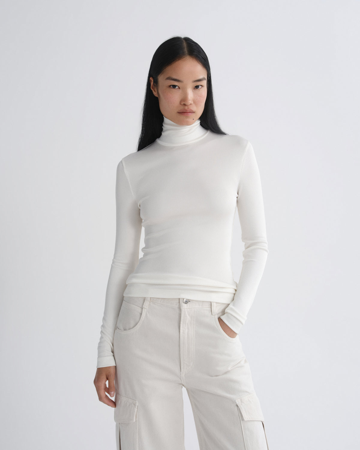Person wearing a white turtleneck and pants on a plain background