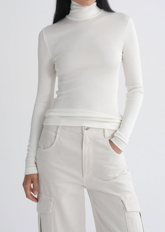 A model wearing a fitted, long-sleeve white turtleneck top and matching off-white cargo pants, shown from the neck down against a grey background.