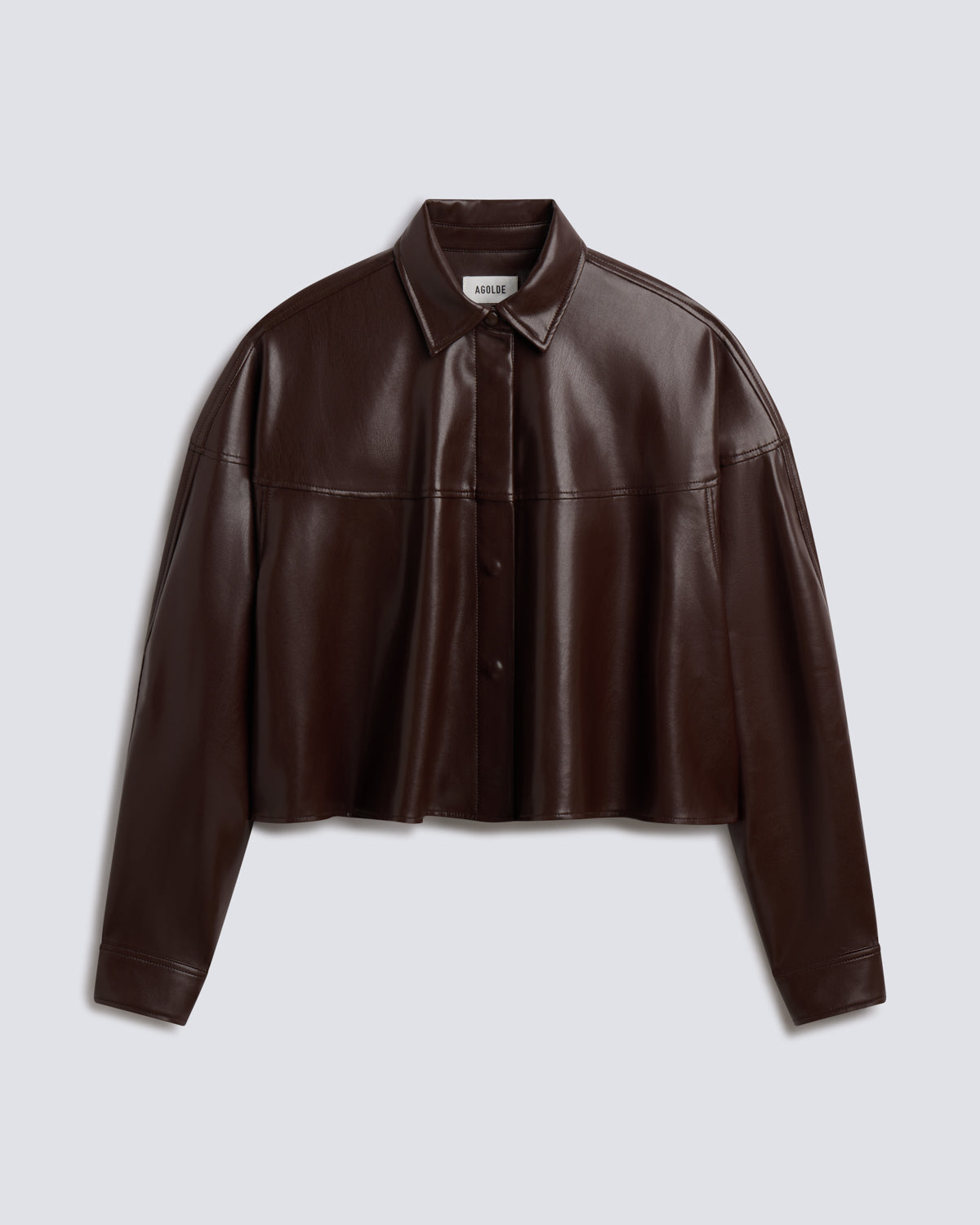 A dark brown faux leather cropped button-up shirt jacket with a collar and long sleeves, displayed on a light gray background.