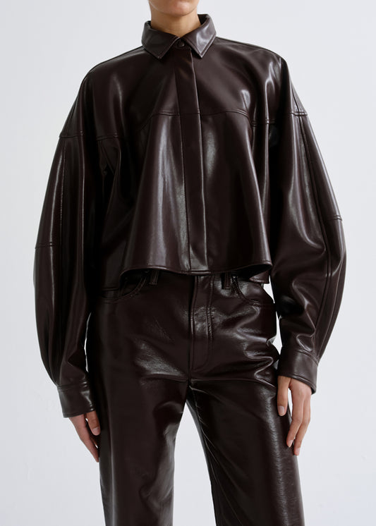 A model wearing a dark brown glossy faux leather cropped button-up shirt and matching wide-leg trousers against a grey background.