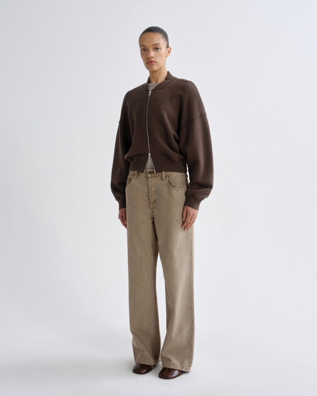 Person wearing a brown jacket and beige pants on a white background