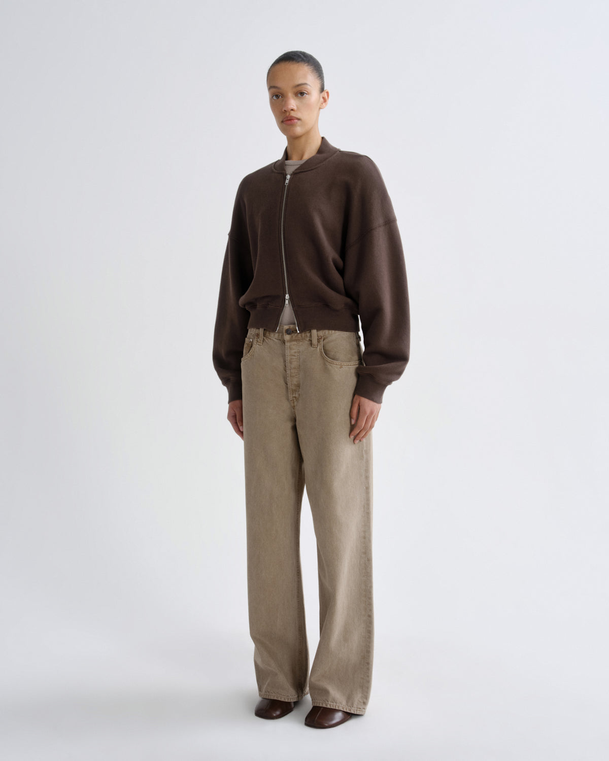 Person wearing a brown jacket and beige pants on a white background