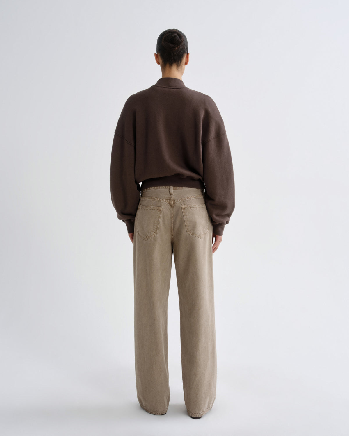 Person wearing a brown sweater and beige pants on a white background