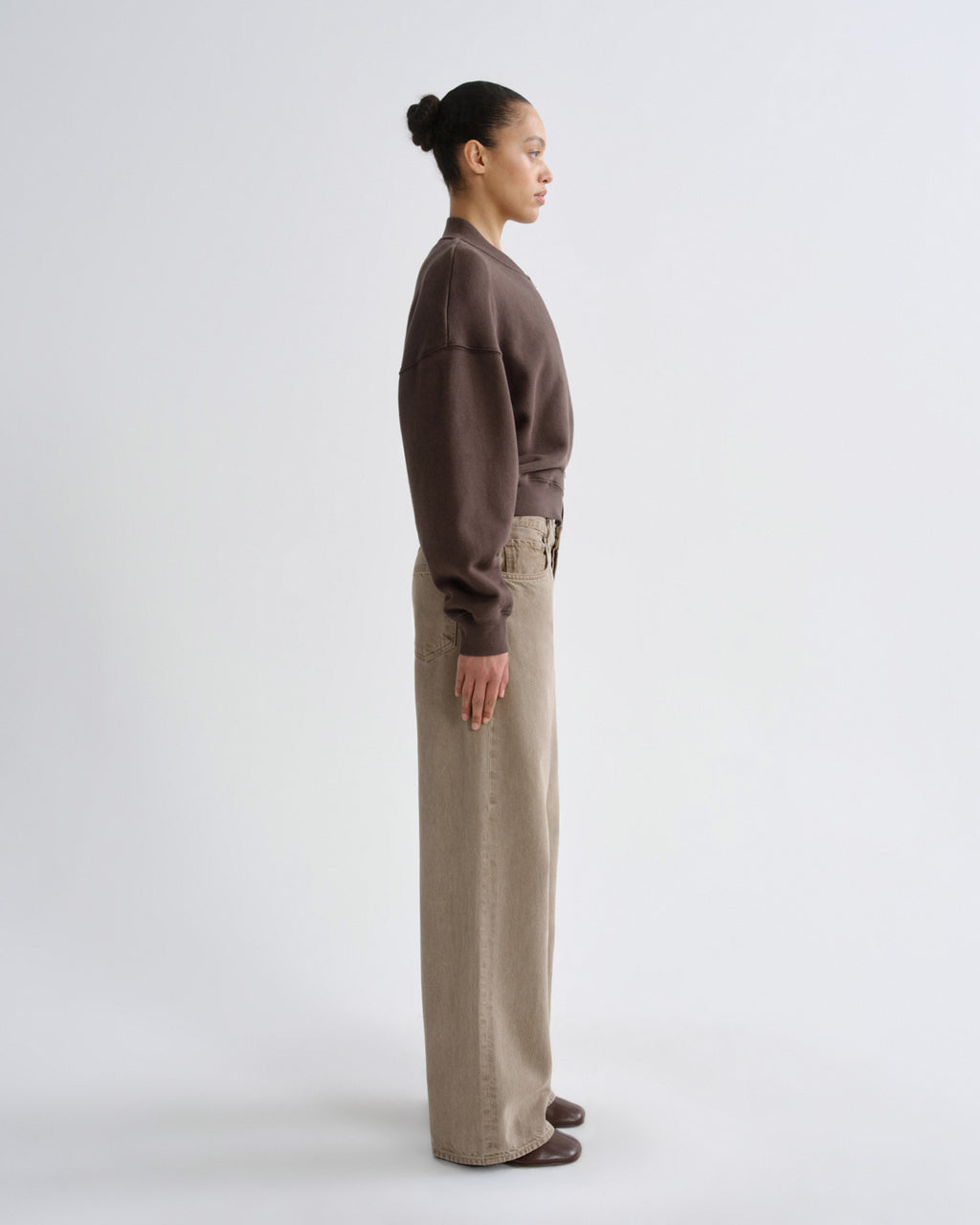 Person wearing a brown sweater and beige pants on a white background