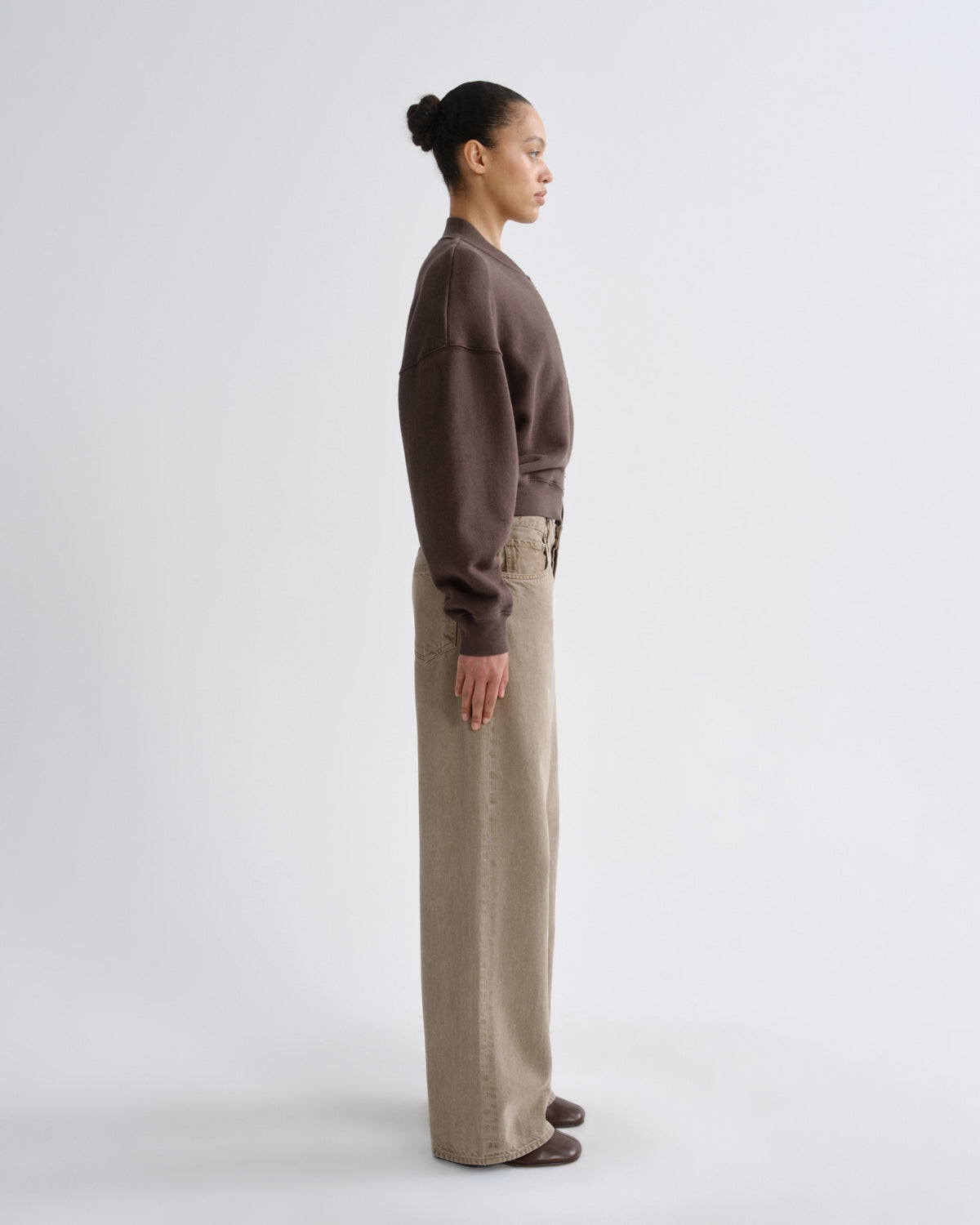 Person wearing a brown sweater and beige pants on a white background