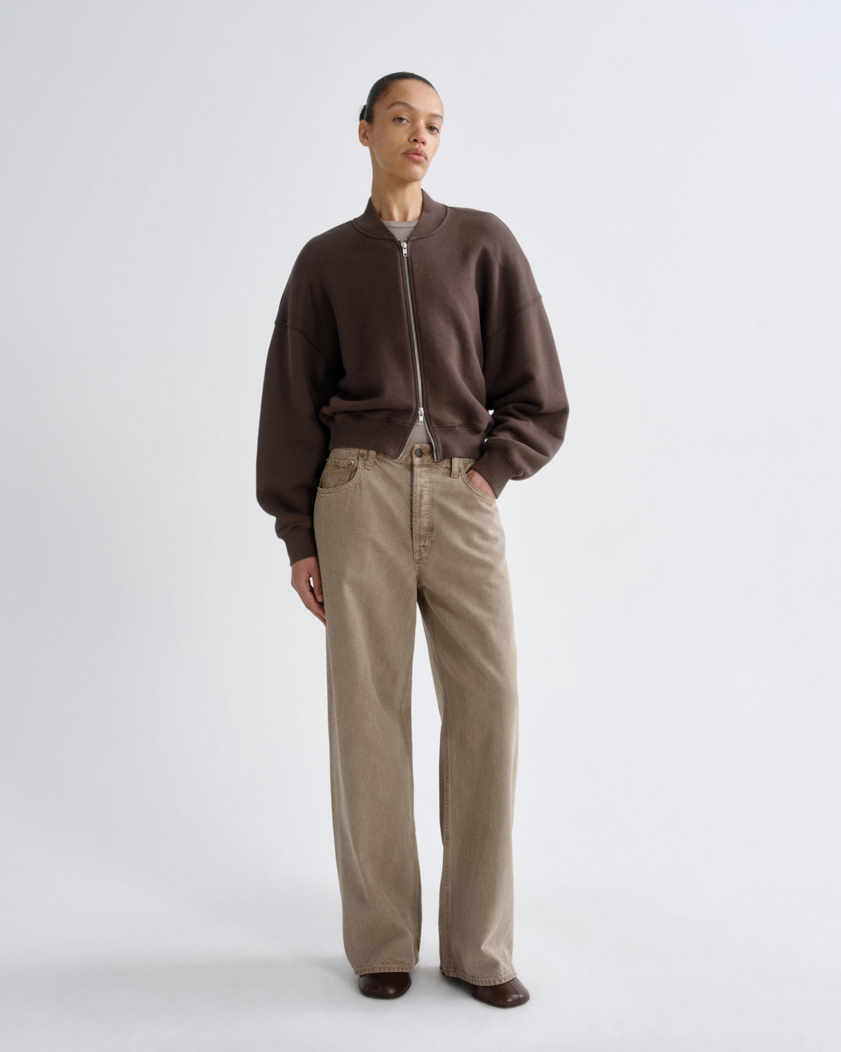 Person wearing a brown sweater and beige pants on a white background