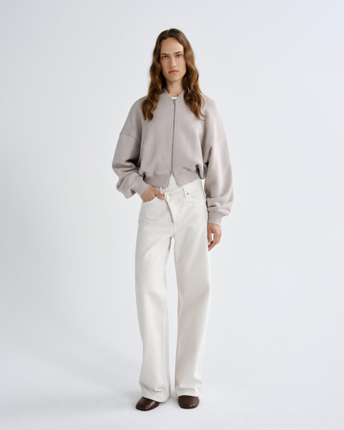 Woman wearing a gray sweater and white pants on a light gray background