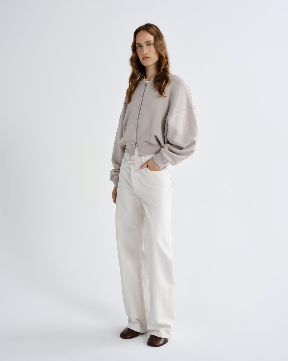 Woman wearing a light gray sweater and white pants on a white background