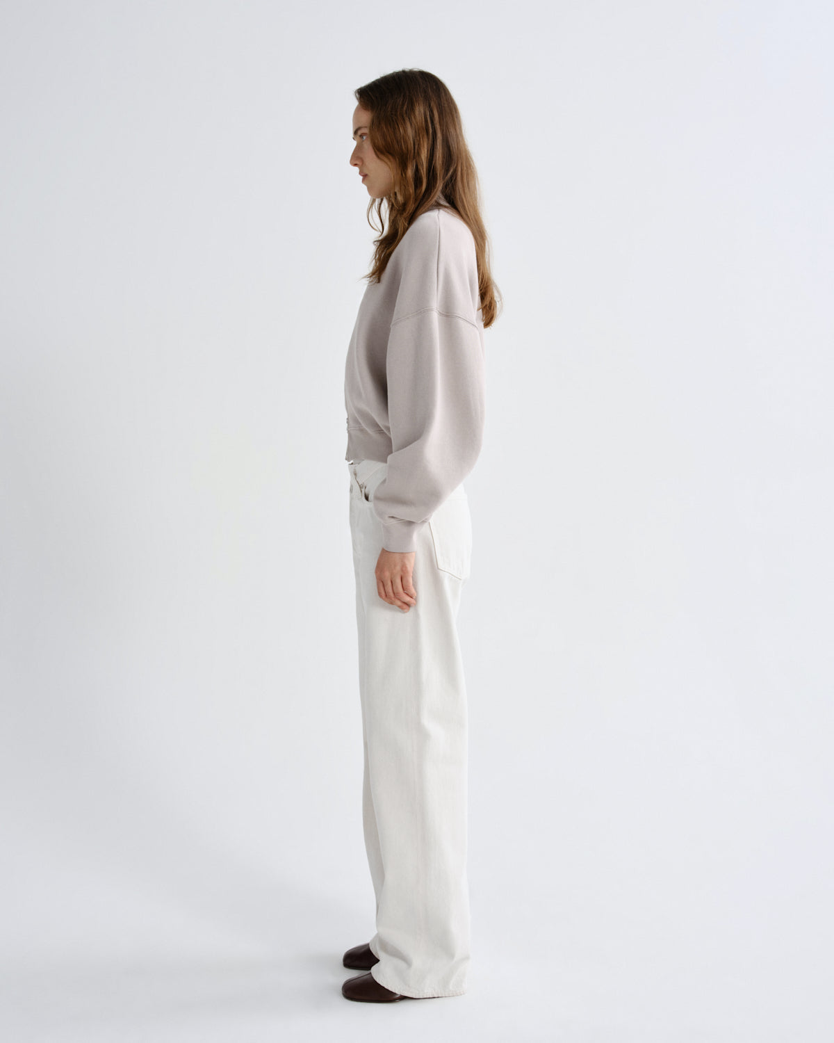 Woman wearing a light gray sweater and white pants on a white background