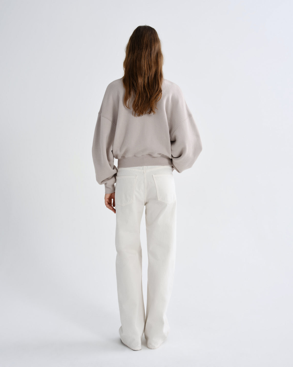 Person wearing a light gray sweater and white pants on a plain background
