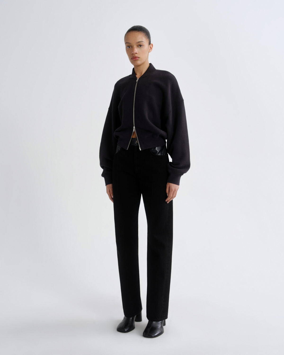 Person wearing a black outfit with a bomber jacket and pants on a white background