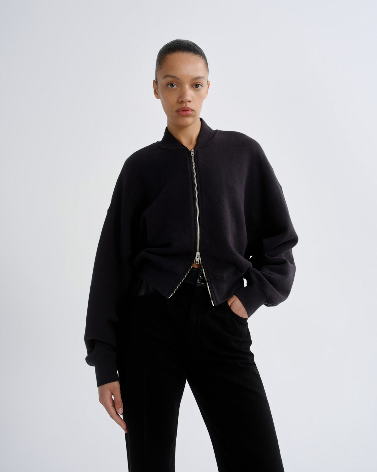 Person wearing a black bomber jacket and pants on a white background