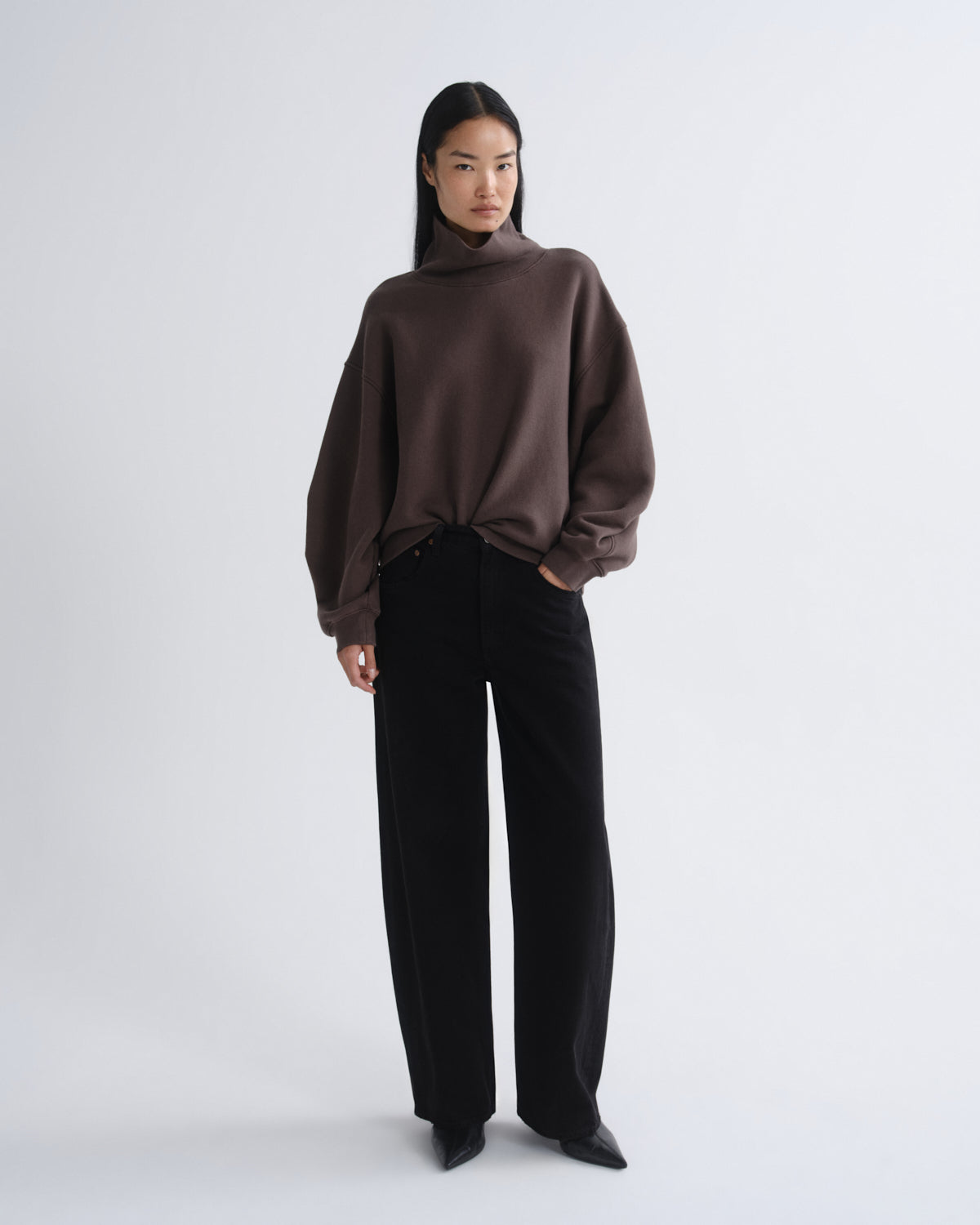 Person wearing a brown sweater and black pants on a white background