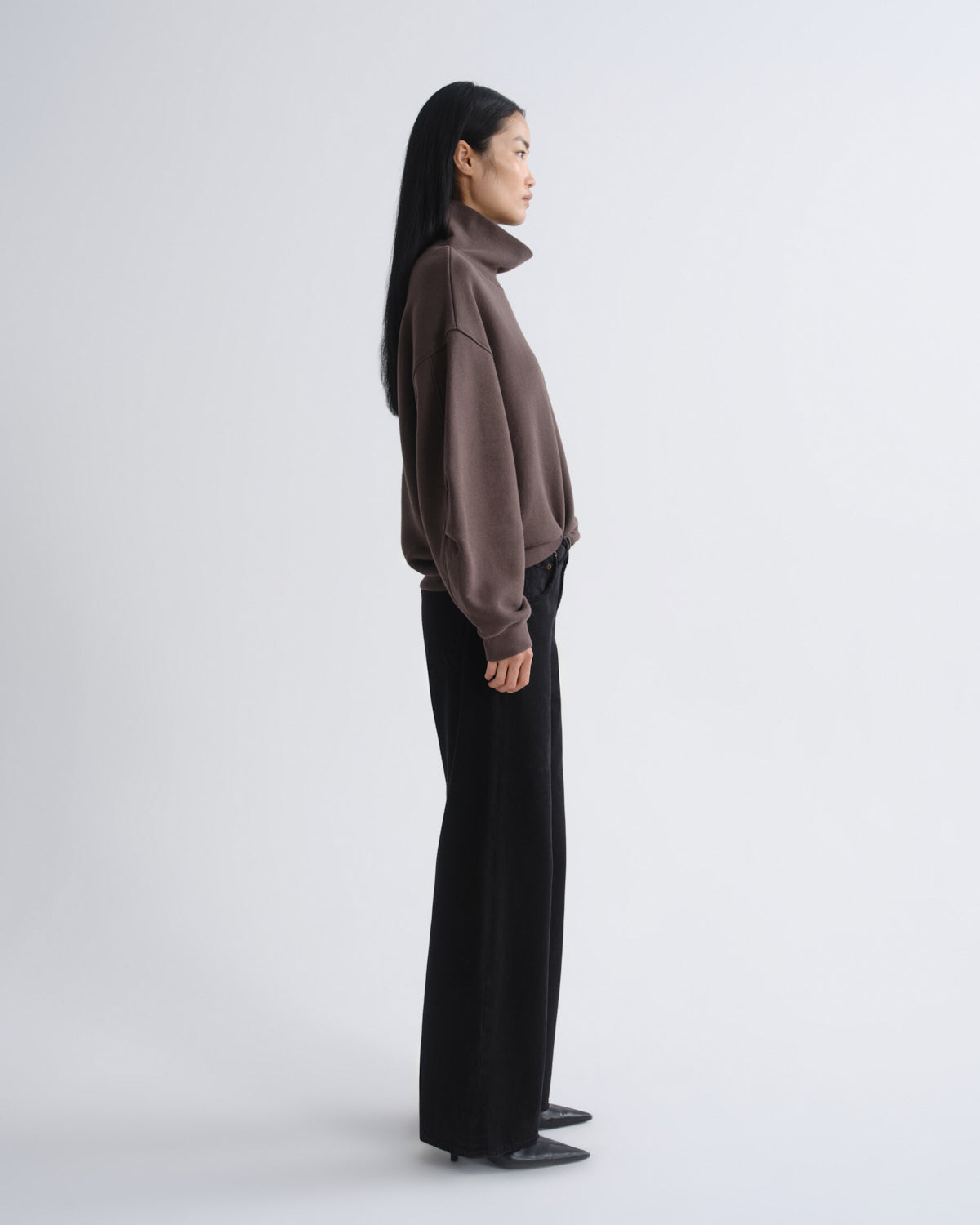 Woman wearing a brown turtleneck and black pants on a white background