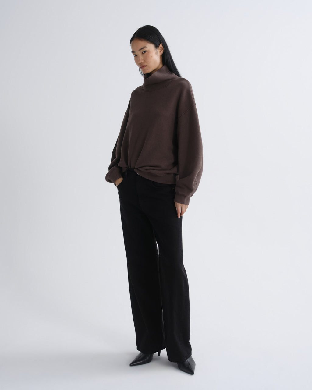 Woman wearing a brown turtleneck and black pants on a white background