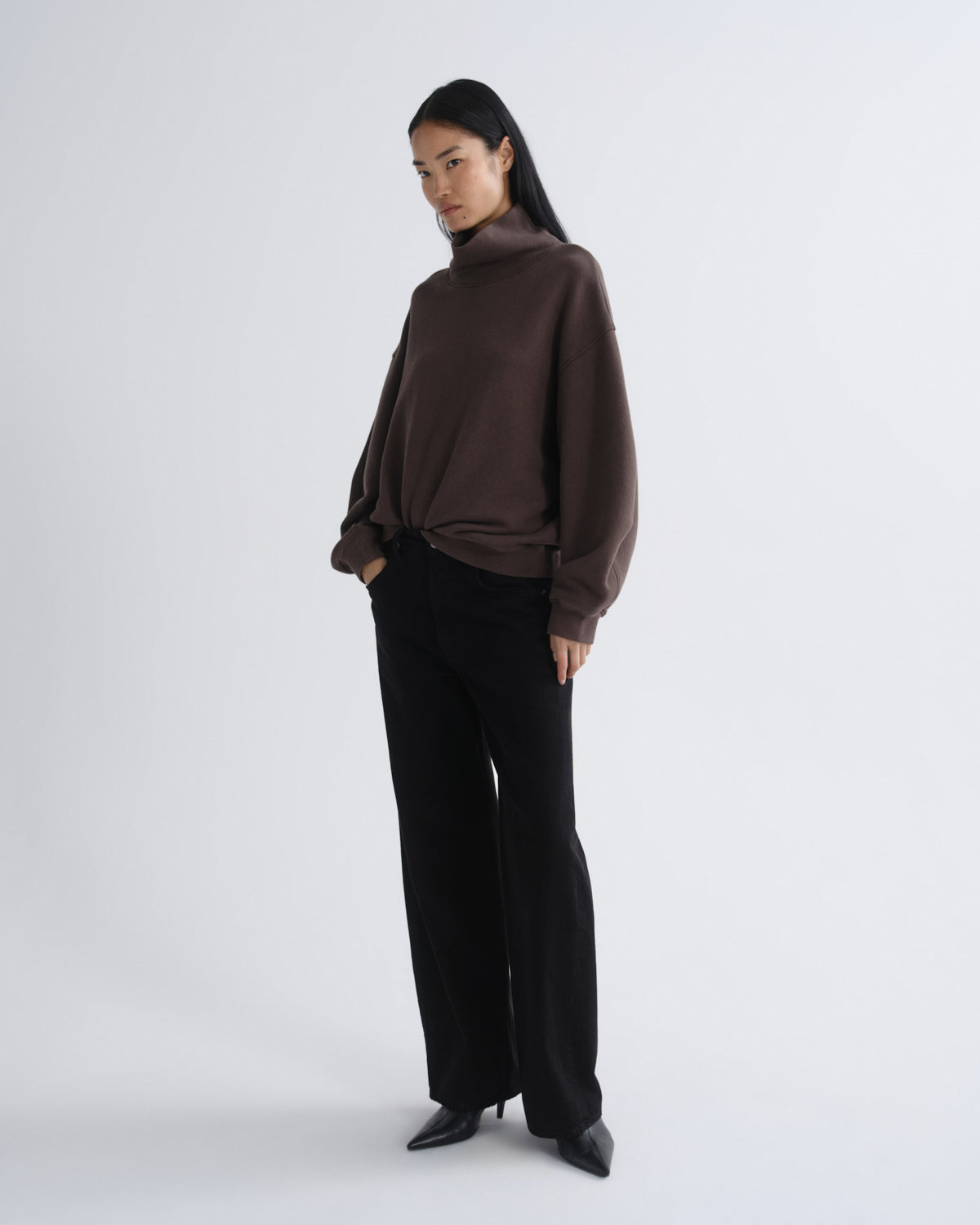 Woman wearing a brown turtleneck and black pants on a white background