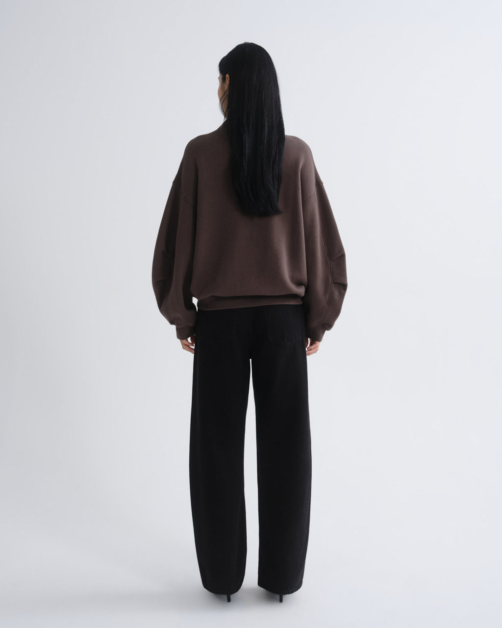 Person wearing a brown sweater and black pants on a white background