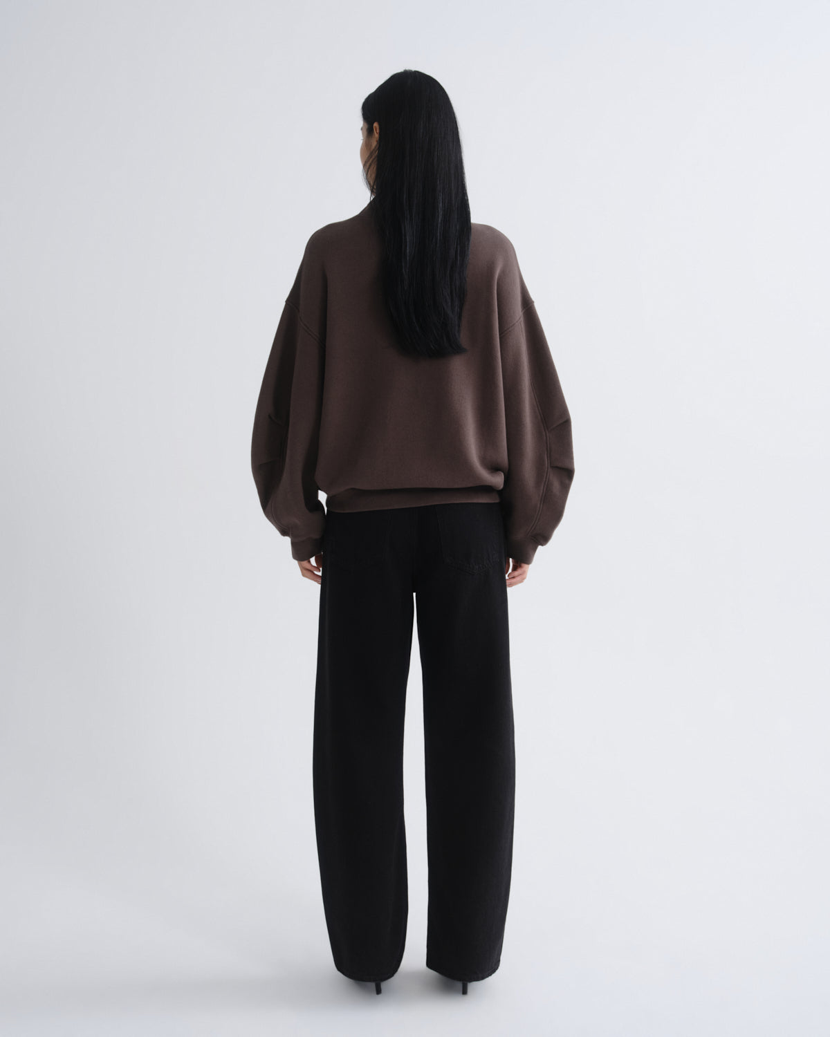 Person wearing a brown sweater and black pants on a white background