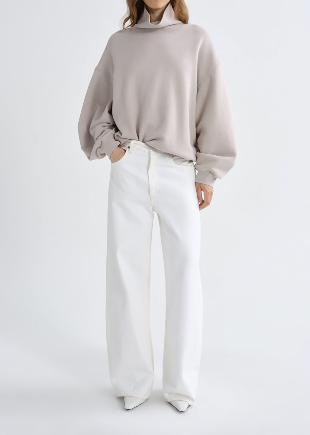 A model shown from the front wearing a light taupe oversized sweatshirt and white wide-leg trousers, set against a grey background.