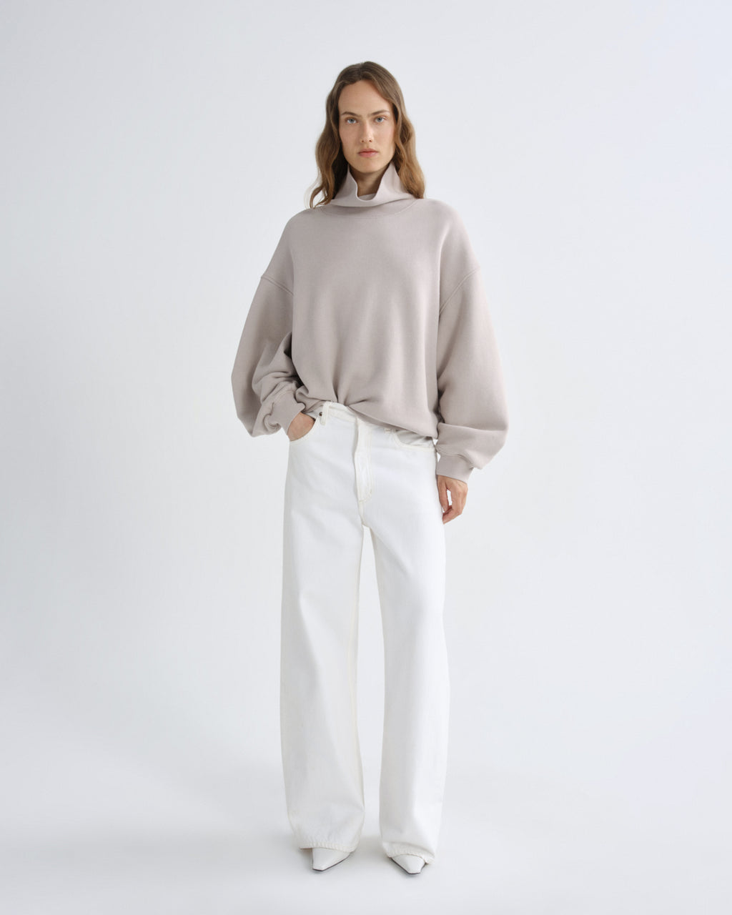 Woman wearing a light gray sweater and white pants on a white background