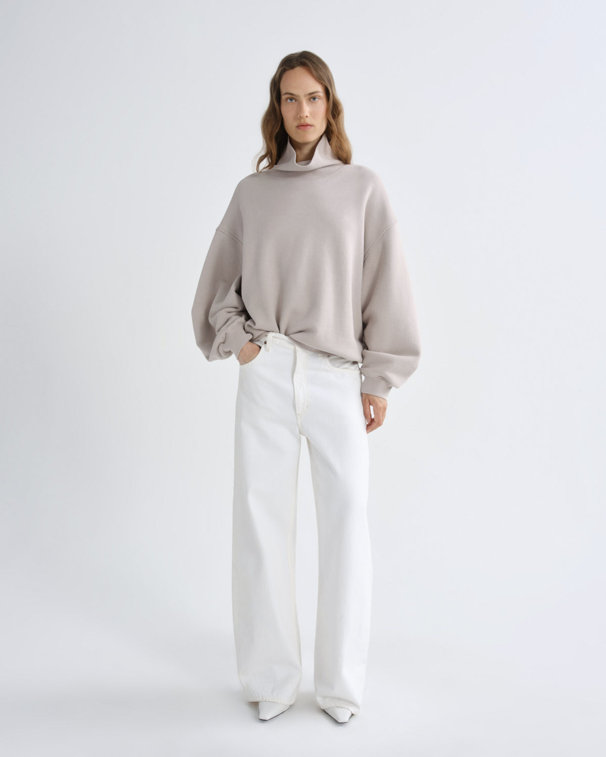 Woman wearing a light gray sweater and white pants on a white background