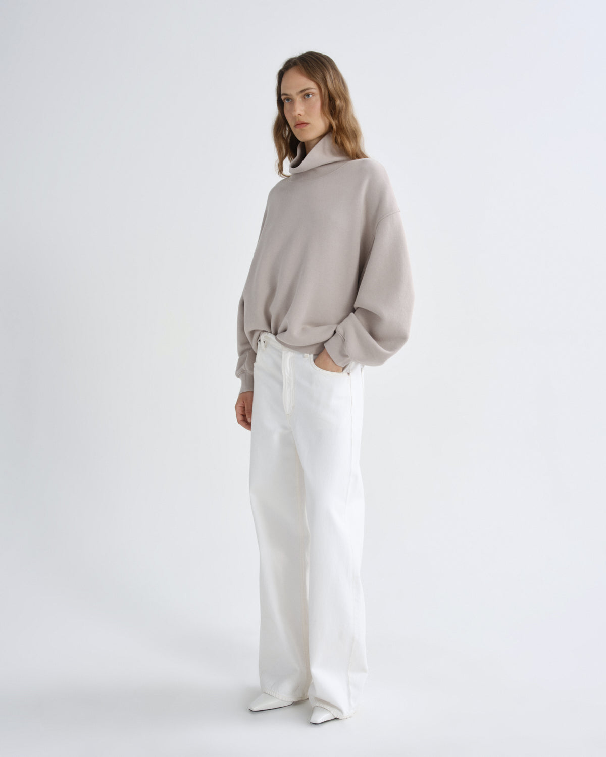 Woman wearing a beige sweater and white pants on a white background