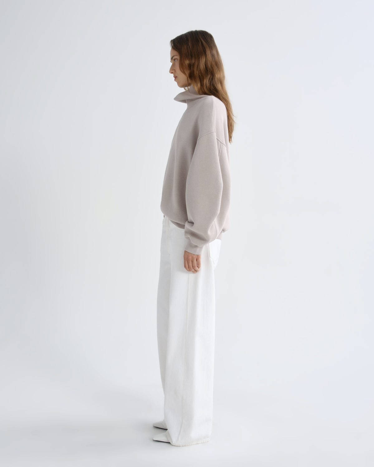 Woman wearing a light gray sweater and white pants on a white background