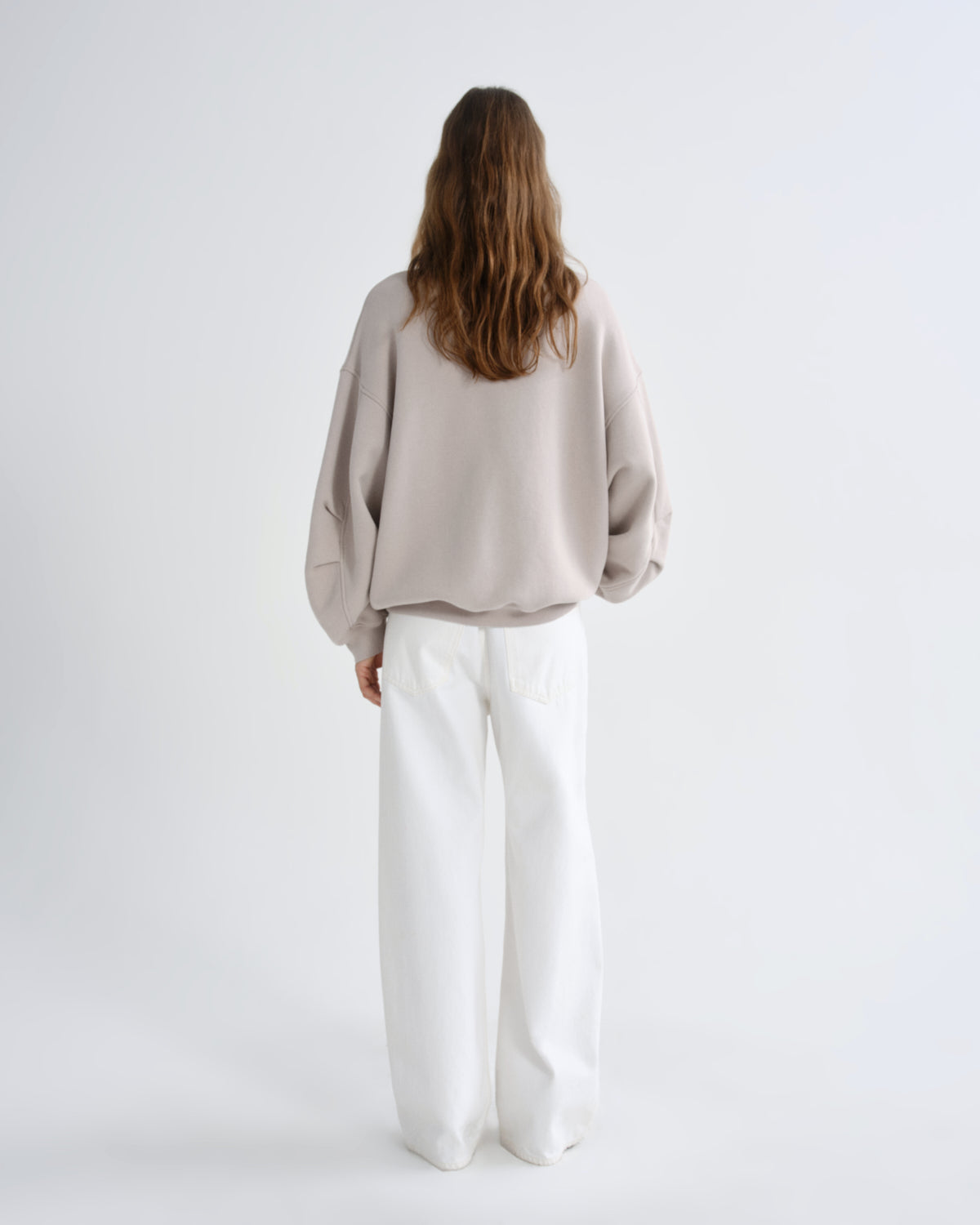 Person wearing a beige sweater and white pants on a light gray background