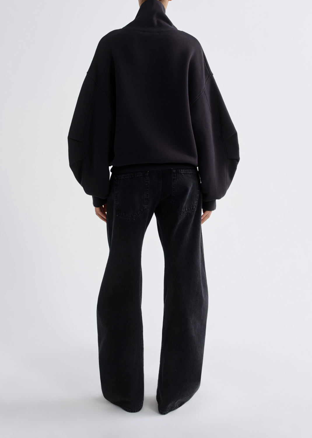 A model shown from the back wearing a black cropped sweatshirt with voluminous balloon sleeves and black wide-leg jeans, set against a grey background.