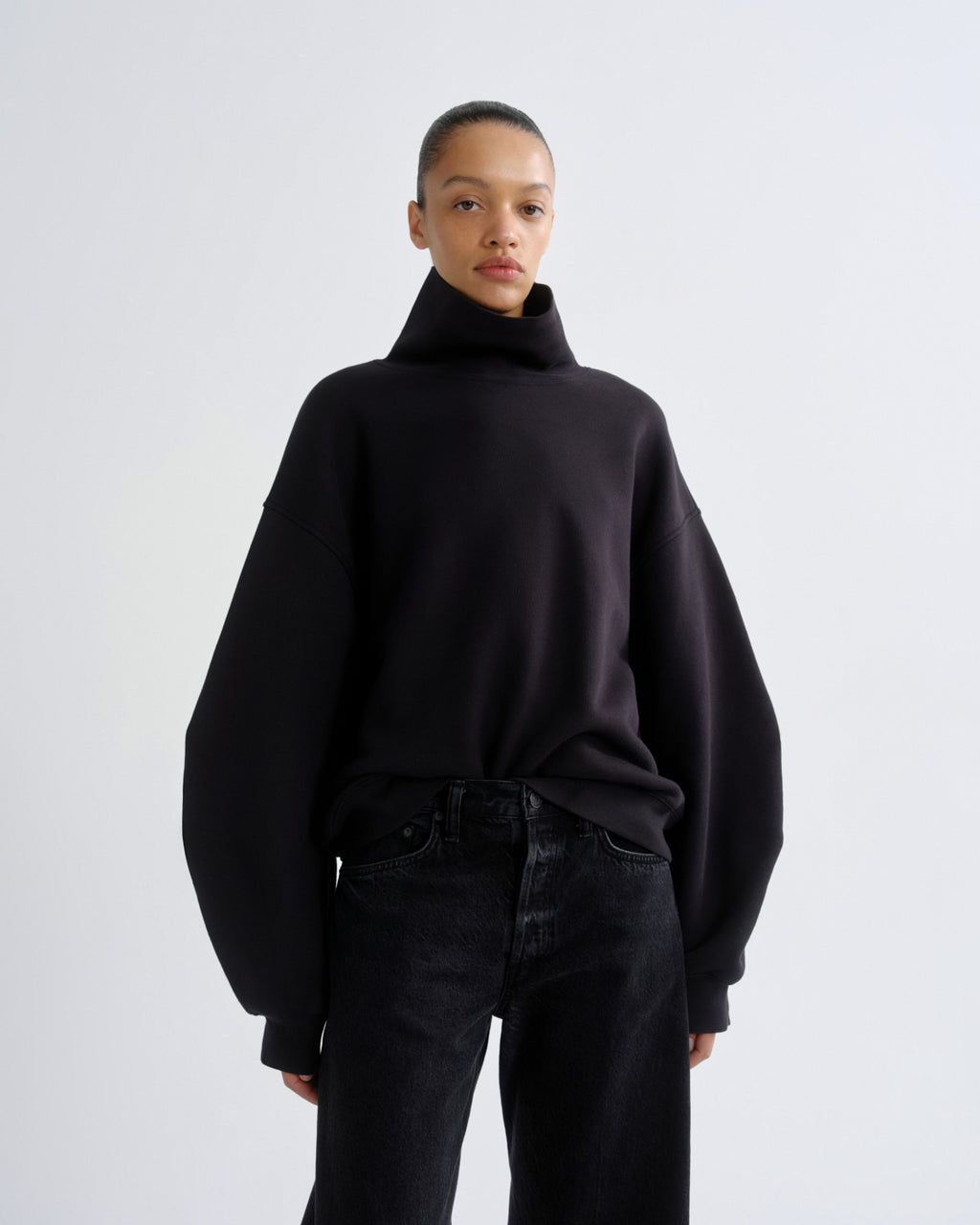 Person wearing a black turtleneck sweater and black pants on a white background