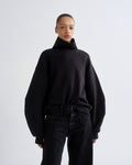 Person wearing a black turtleneck sweater and black pants on a white background