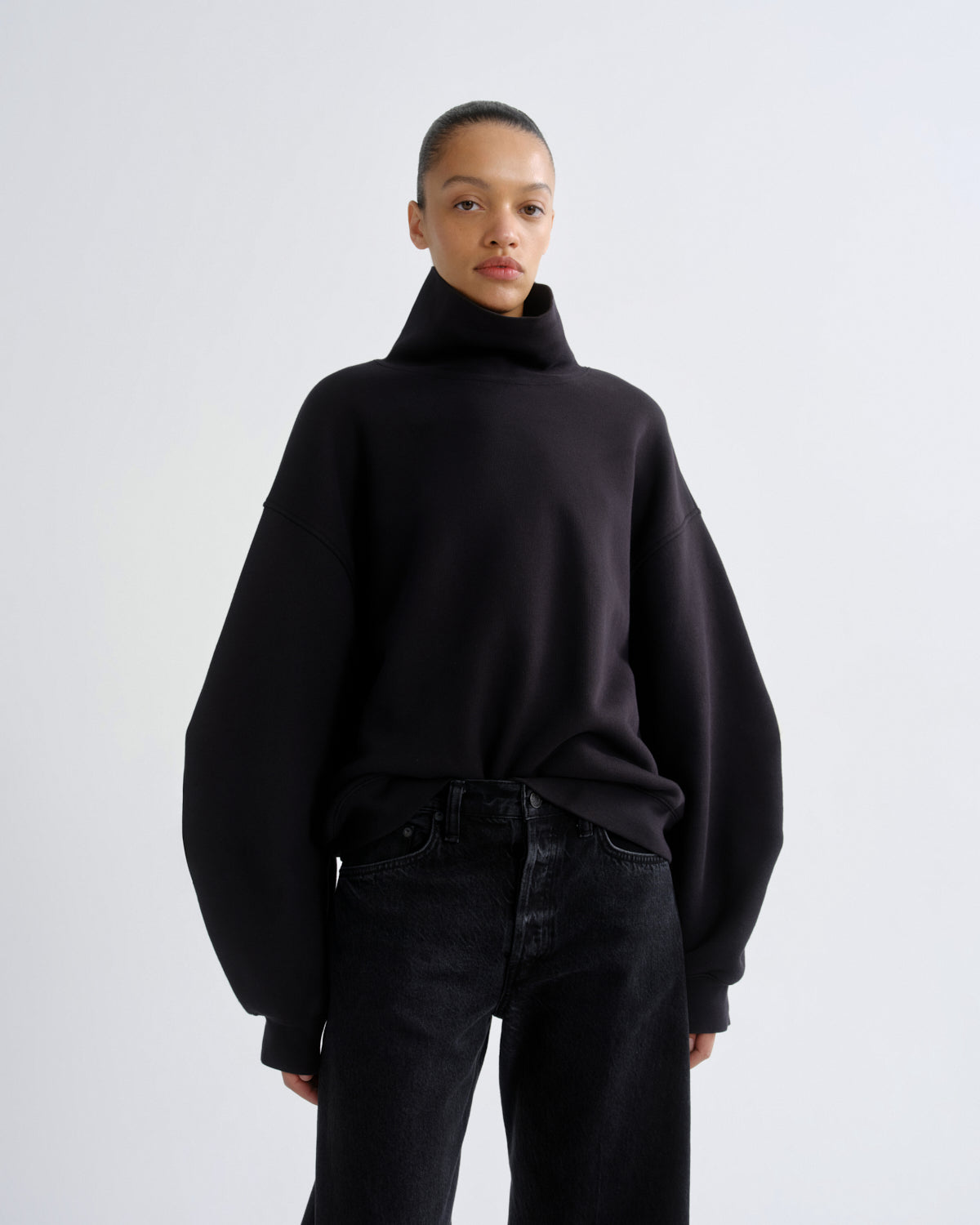 Person wearing a black turtleneck sweater and black pants on a white background