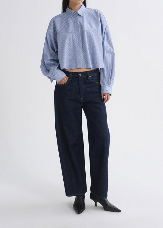 Person wearing a blue striped shirt and dark jeans on a grey background