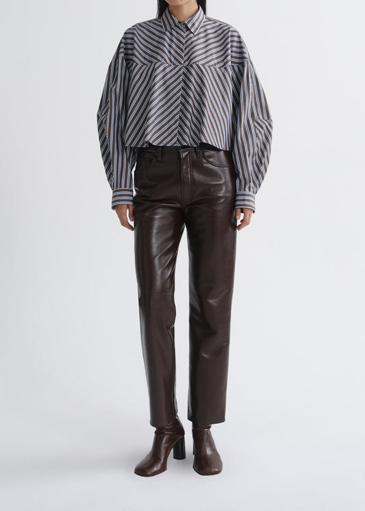A model wearing a cropped, long-sleeve button-up shirt with diagonal grey and black stripes, paired with dark brown faux-leather trousers and matching brown heeled ankle boots, shot against a grey background.