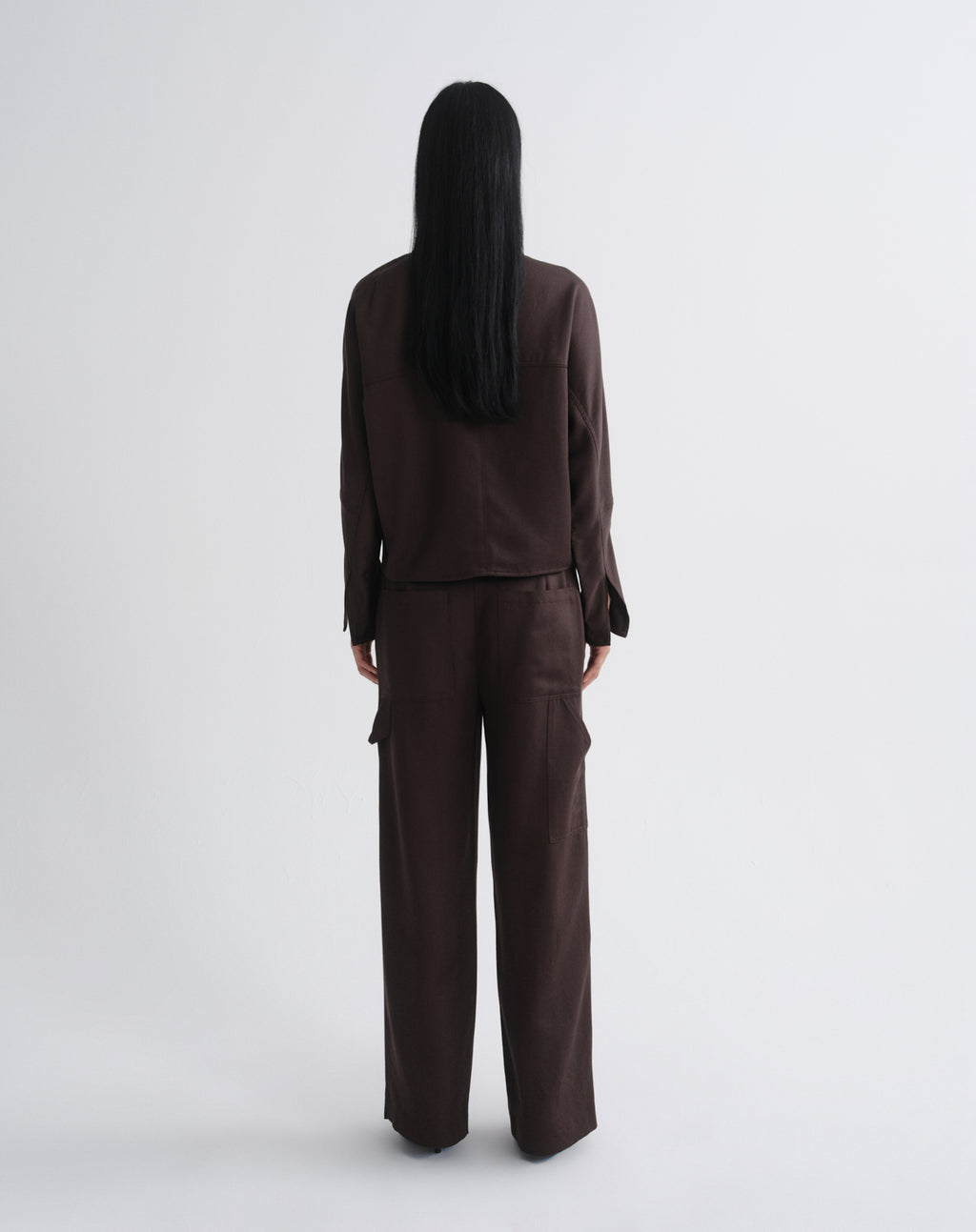 A model viewed from the back wearing a dark brown long-sleeve cropped top and matching wide-leg cargo pants against a grey background.