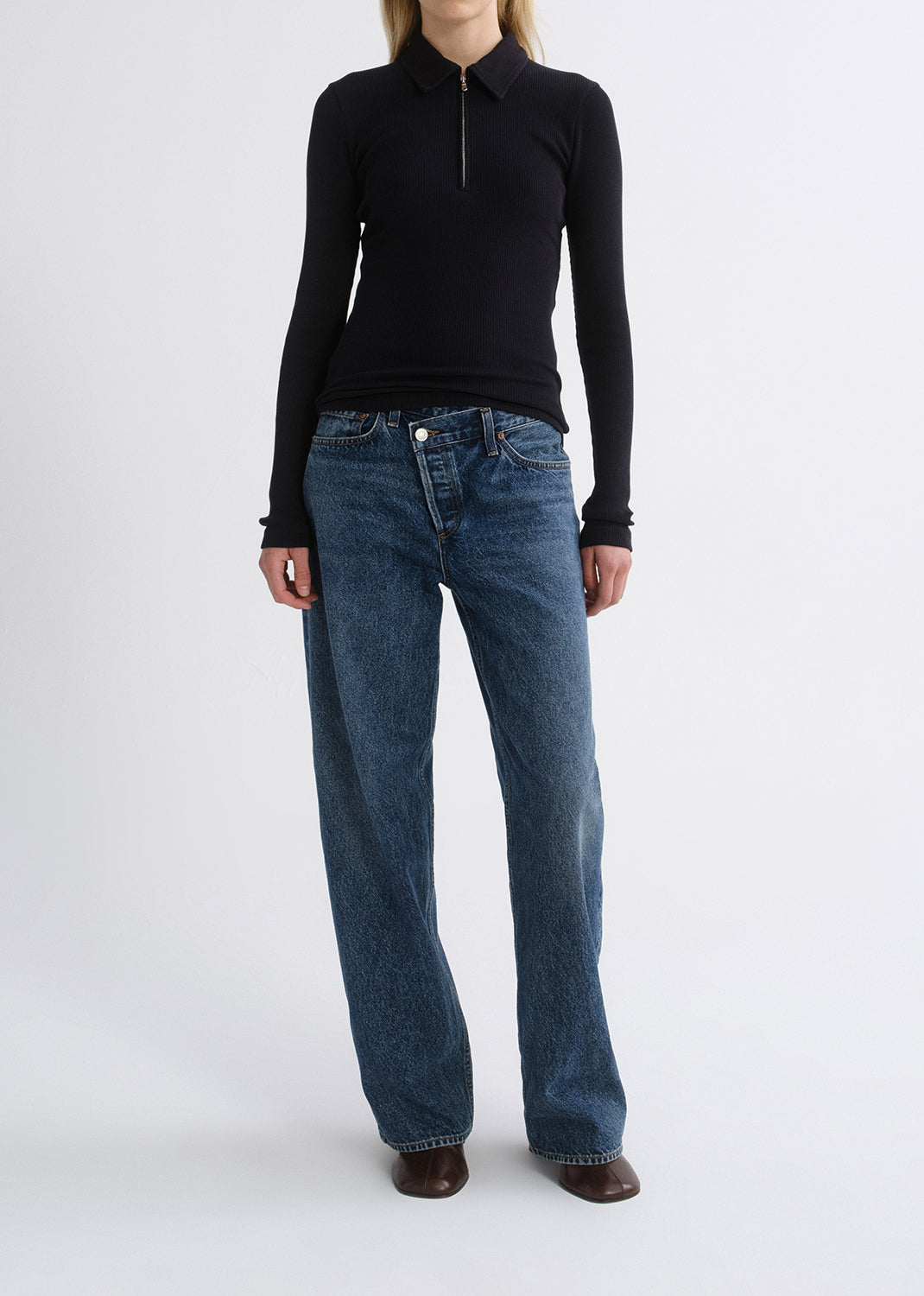 Person wearing a black fitted half-zip top with medium blue straight leg jeans on a grey background