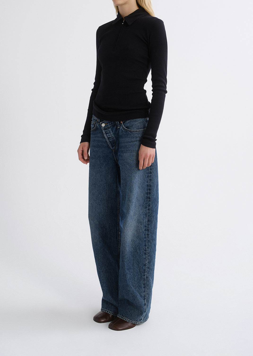 Person wearing a black fitted half-zip top with medium blue straight leg jeans on a grey background