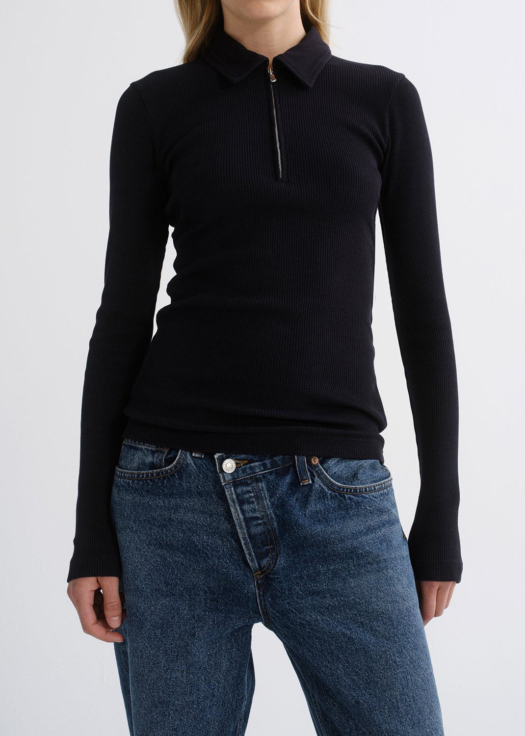 Person wearing a black fitted half-zip top with medium blue straight leg jeans on a grey background