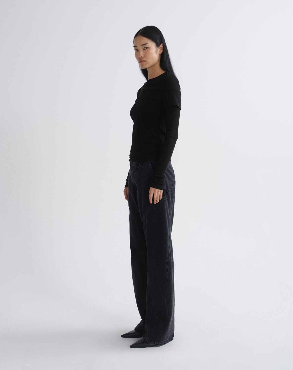 Person wearing a black layered short sleeve top with black wide leg pants viewed from the side on a grey background