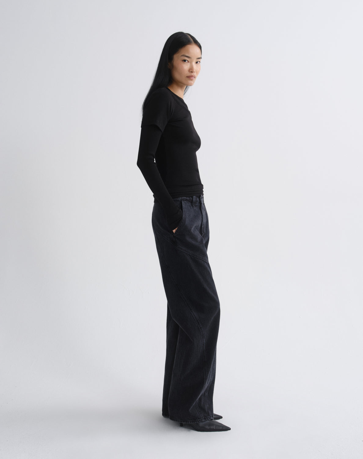 Person wearing a black layered short sleeve top with black wide leg pants viewed from the side on a grey background