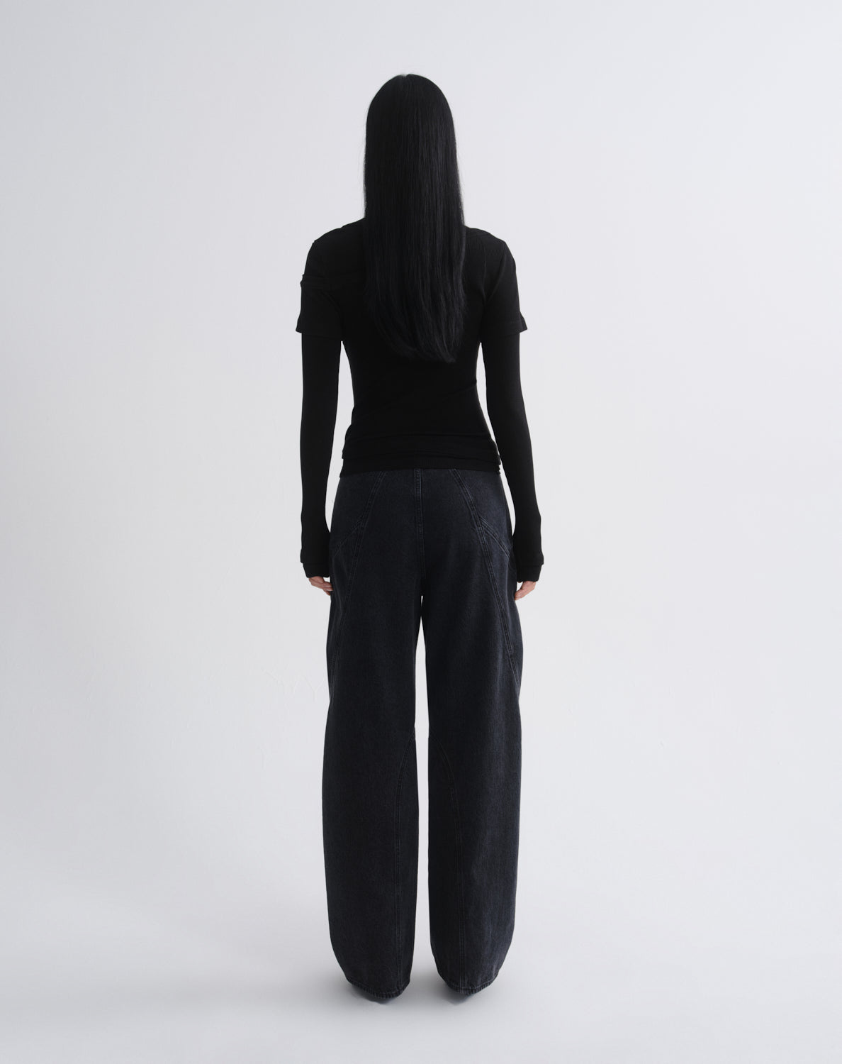 Person wearing a black layered short sleeve top with black wide leg pants viewed from the back on a grey background