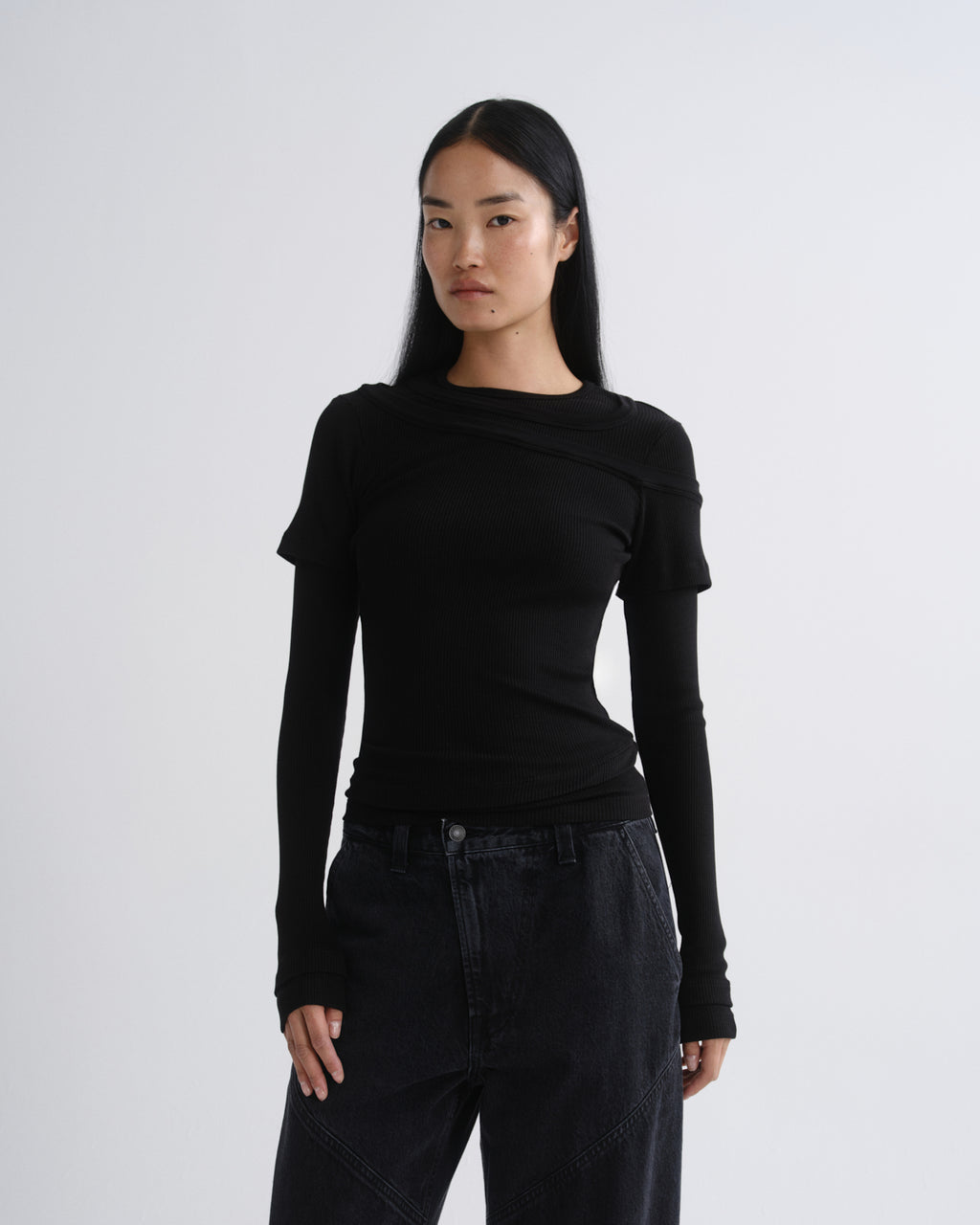 Person wearing a black layered short sleeve top with black wide leg pants on a grey background