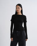 Person wearing a black layered short sleeve top with black wide leg pants on a grey background