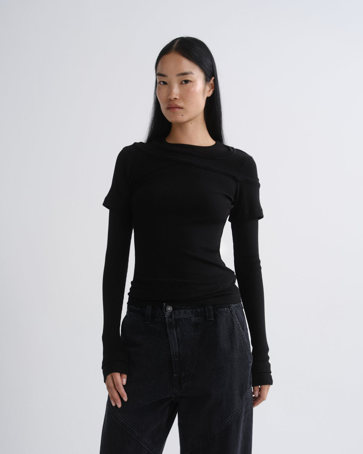 Person wearing a black layered short sleeve top with black wide leg pants on a grey background